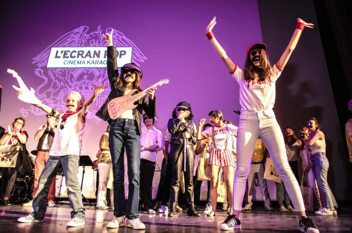 Un groupe en costume se produit sur la scène du Cinéma Karaoké à Lille, avec des lumières violettes et le logo "L'Écran Pop" qui brille derrière.