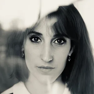 Portrait en noir et blanc d'une femme aux cheveux mi-longs, regardant directement l'appareil photo à travers une surface vitrée.