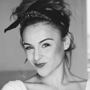 Femme au bandeau bandana, légèrement souriante, portant un haut blanc, photographiée en noir et blanc.