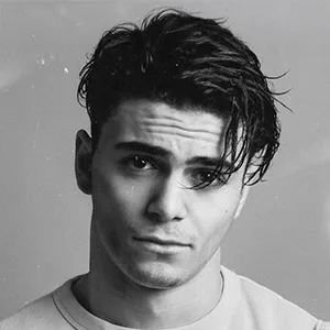 Portrait en noir et blanc d'un jeune homme aux cheveux sombres et ébouriffés, regardant légèrement vers le haut avec une expression neutre.