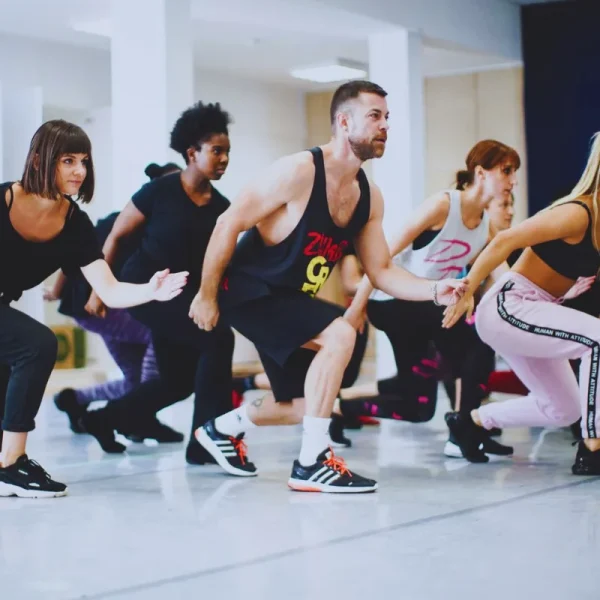 Un groupe d'adultes en tenue de sport exécute une chorégraphie synchronisée dans un studio lumineux.