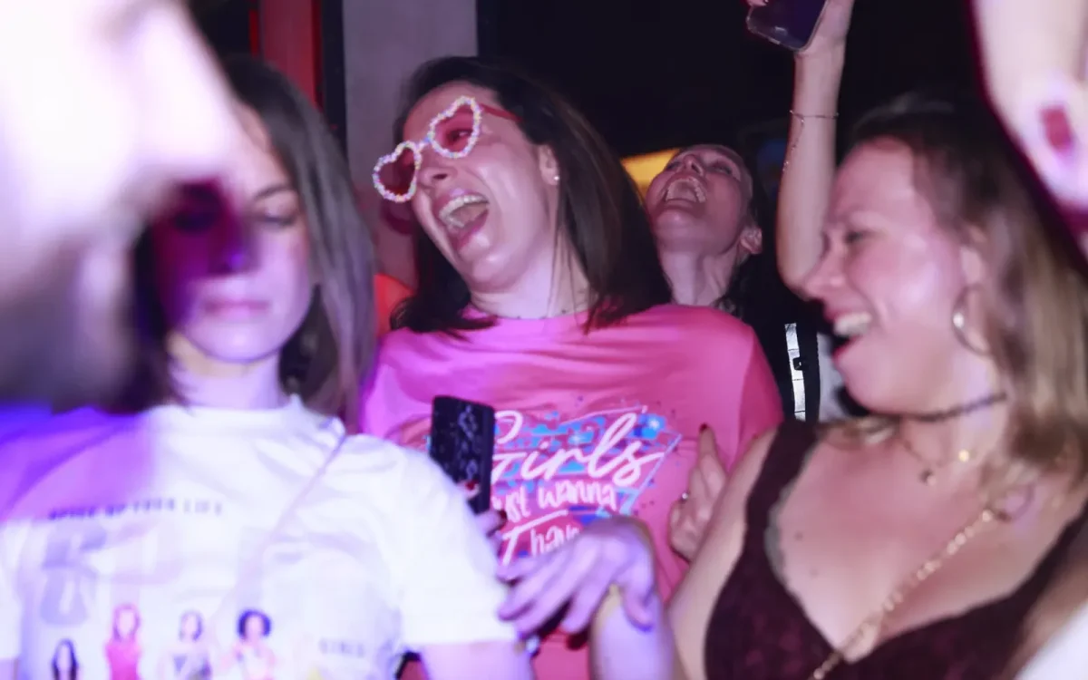 Plusieurs femmes rient et dansent lors d'une soirée animée dans un club parisien, profitant d'un éclairage coloré inspiré des années 80/90/2000.